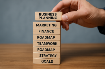 small business growth plan: close-up of a hand stacking wooden blocks labelled Goals, Strategy, Roadmap, Teamwork, Finance, Marketing, Business Planning, symbolising steps for small business growth.