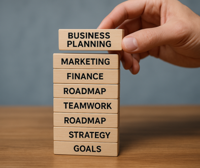 small business growth plan: close-up of a hand stacking wooden blocks labelled Goals, Strategy, Roadmap, Teamwork, Finance, Marketing, Business Planning, symbolising steps for small business growth.