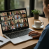 online networking: A small business owner participates in a Zoom BNI video call with international contacts. Her laptop screen shows a grid of diverse professionals from different countries, with a notepad and coffee on the desk, symbolising online networking across borders.